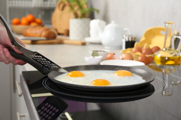 Woman cooking eggs in frying pan on cooktop indoors, closeup