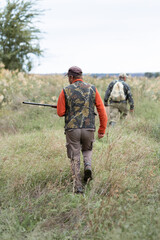 Mature hunter man holding a shotgun and walking through a field