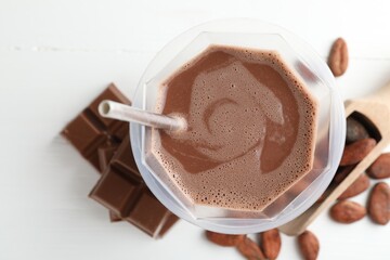 Tasty chocolate milk, bars and cocoa beans on white wooden table, flat lay