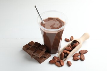Tasty chocolate milk, bars and cocoa beans on white wooden table