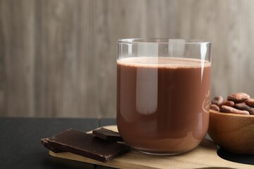 Tasty chocolate milk, bars and cocoa beans on black wooden table, closeup. Space for text