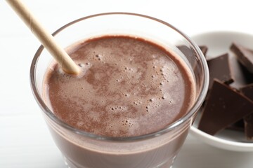 Tasty chocolate milk and pieces on white table, closeup