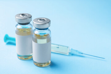 Hepatitis vaccine in glass vials and syringe on light blue background, closeup