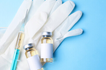 Hepatitis vaccine in glass vials, syringe and medical gloves on light blue background, top view