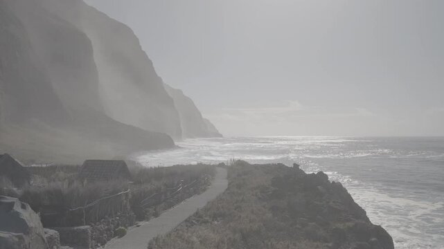 Misty coastal cliffs of Madeira with crashing waves and sunlight reflecting on Atlantic Ocean (SLOG3)