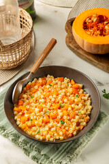 Homemade vegan pasta ditalini with pumpkin, squash sauce in a dark plate,  cooked with rosemary and parsley on a beige table. Vertical image.