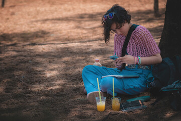 Young woman is holding her cell phone, she is sitting in the forest.
