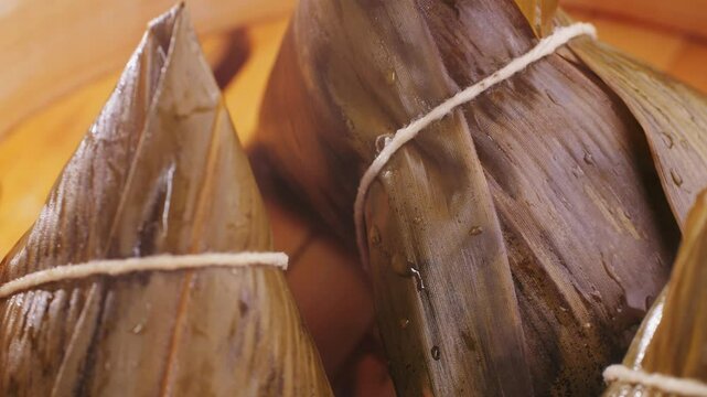 Hand holding zongzi (rice dumpling) with savoury fillings wrapped in bamboo or reed leaves.