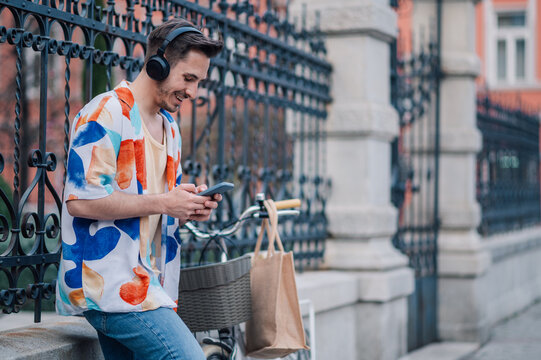 Stylish man using smartphone and listening music with headphones and bicycle