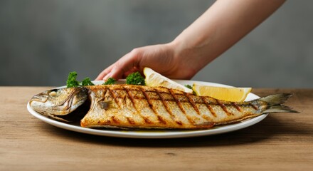 Grilled whole fish on plate with lemon and parsley on wooden table