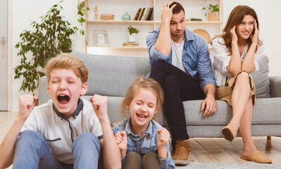 Kids Misbehavior. Parents Sitting Exhausted While Children Shouting And Crying Loudly Having...