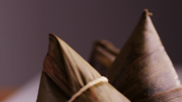 Hand holding zongzi (rice dumpling) with savoury fillings wrapped in bamboo or reed leaves.