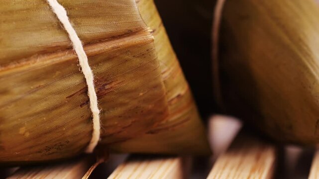 Hand holding zongzi (rice dumpling) with savoury fillings wrapped in bamboo or reed leaves.
