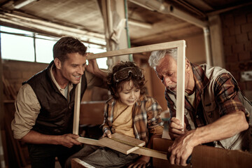 Fototapeta premium Three male generations working together on a woodworking project in family workshop