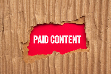 Paid content message written on ripped torn cardboard paper on red background. Conceptual paid...