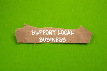 Support local business message written on ripped torn brown paper piece on green background....