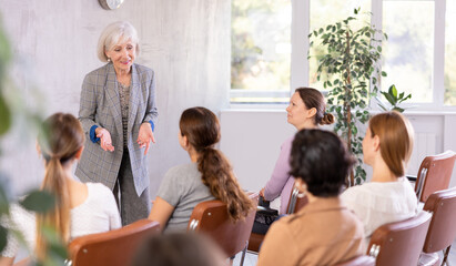 Emotional aged female tutor leading educational class for group of women sitting in auditorium..