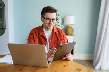 Engaged Young Man Working on a Tablet While Seated at a Wooden Table in a Bright Modern Room