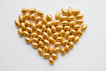 Gold foil wrapped chocolate eggs arranged in heart shape on white background