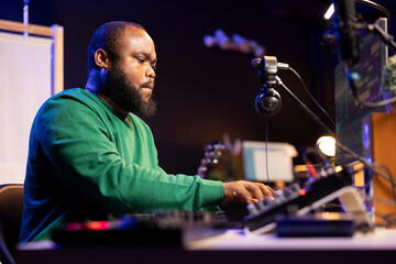 Songwriter mixing and mastering tracks on stereo console, playing electronic keyboard in home studio. Artist oversees audio performances to ensure the perfect melody, producing tunes with piano keys.