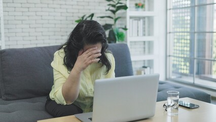 Elderly Asian woman suffers from headache from working too hard on laptop