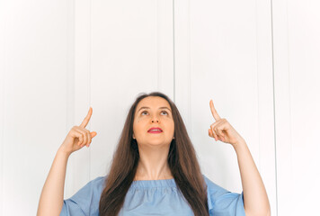 A young, attractive girl looking up and pointing with index finger at copy space. A sign, an empty space for advertising, inscription, design. White background.