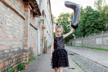 A happy girl in an elegant black dress with balloons celebrates the Birthday. Fashion stylish concept
