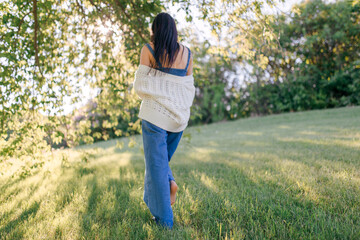 A young pretty woman is walking barefoot on the green grass. Sunny summer day outdoors. Back view