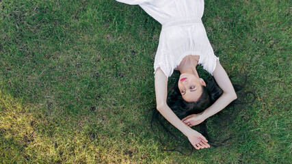 A young, pretty woman is lying on the green grass resting. Top view, copy space
