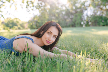 A young, pretty woman is lying on the green grass resting. Summer sunny day, nature lover, enjoying time outside