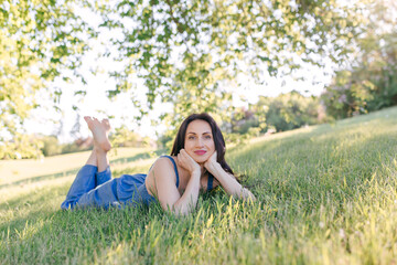 A young, pretty woman is lying on the green grass resting. Summer sunny day, nature lover, enjoying time outside
