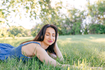 A young, pretty woman is lying on the green grass resting. Summer sunny day, nature lover, enjoying time outside