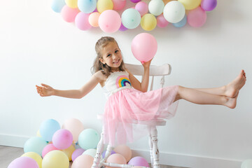 A little happy girl in dress with colorful balloons on a white background, studio shoot. Celebrations, birthday and playing concept.