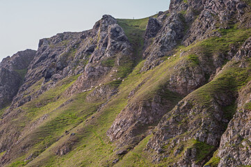 A mountain with a green hillside and a person walking on it