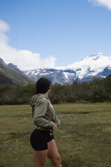 Fototapeta premium brunette long hair woman training in the hills looking back in mountain landscape with green hoodie and black sports shorts