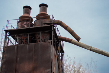 Rusty smokestacks rise above an old factory structure surrounded by sparse vegetation, reflecting a...