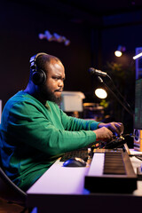 African american music producer twisting knobs on mixing console, producing new tracks with sound effects. Artist composing songs in post production, operates on digital software in home studio.