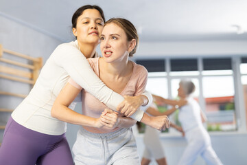 Emotional young woman trying to escape from back grip and delivering elbow strike to midsection to...