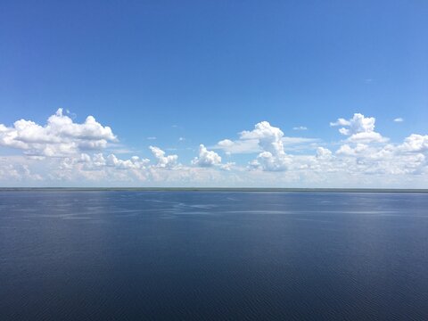 Clear blue sky with scattered clouds over calm lake horizon