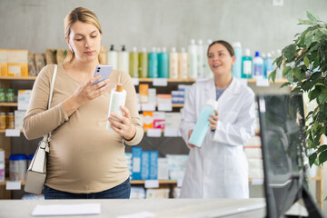 Pregnant woman scanning qr code for shampoo with woman pharmacist in pharmacy