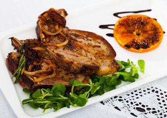 Grilled pork meat on bone with fried orange and onion, served with green corn salad..