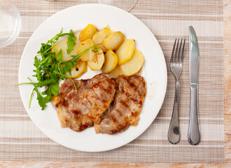 Delicious fried pork with potatoes and fresh arugula served on platter