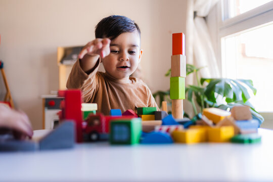 Naklejki Young child building a tower with colorful wooden blocks, developing fine motor skills and creativity in a playful home environment