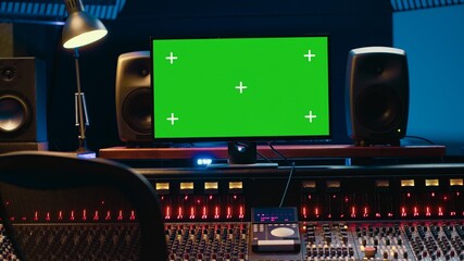 Control room with greenscreen running on computer next to buttons and sliders, multiple controls...