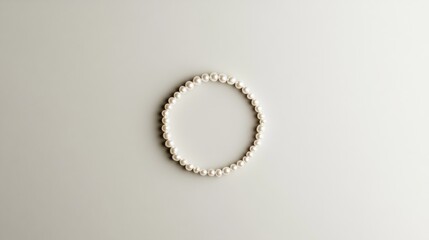 A minimalist composition of a pearl bracelet arranged in a circular shape against a clean white background