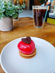 Postre dulce en forma de corazón sobre una galleta, acompañado de un vaso de café caliente.