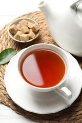 Aromatic black tea and brown sugar cubes on white wooden table, closeup