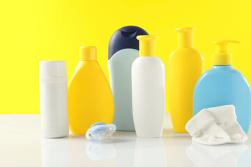Baby cosmetic products, socks and pacifier on table against yellow background