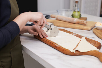 Woman cutting dough at light marble table indoors, closeup. Making croissants