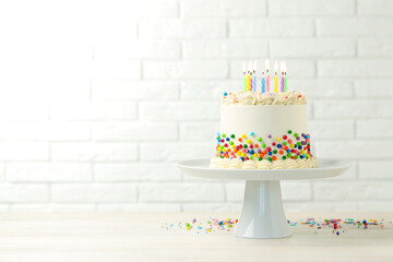 Delicious bento cake with colorful sprinkles and burning candles on light wooden table against...